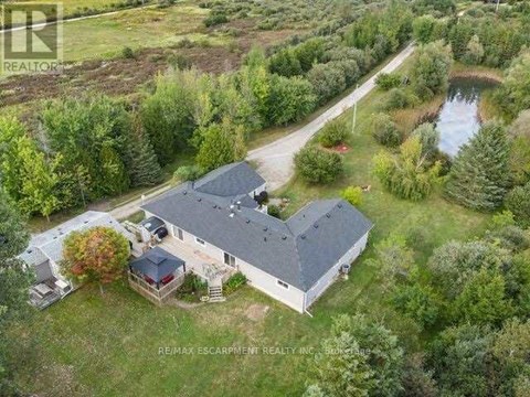 A bird's eye view of a house surrounded by trees and a pond.
