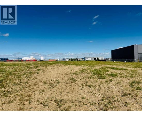 A field with buildings in the distance under a blue sky.