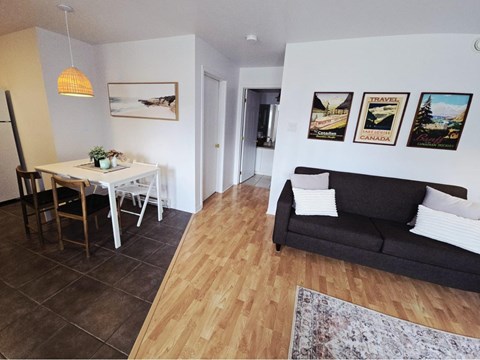 A living room with a couch, a dining table with chairs, and pictures on the wall.