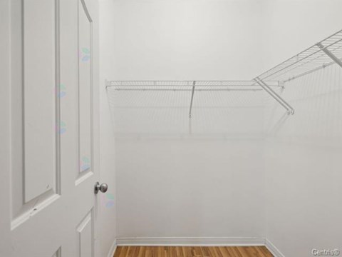 A white door with a silver handle is on the left side of a room with a white wall and a wooden floor.