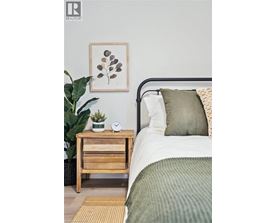 A bedroom with a bed, a nightstand with a plant, and a framed picture on the wall.