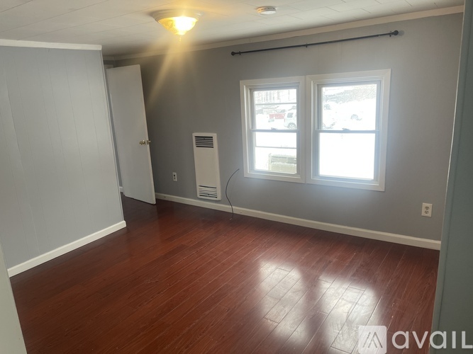 A room with wooden floors and a window showing a parking lot outside.
