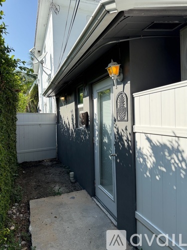 A white house with a grey door and a lamp on the wall.