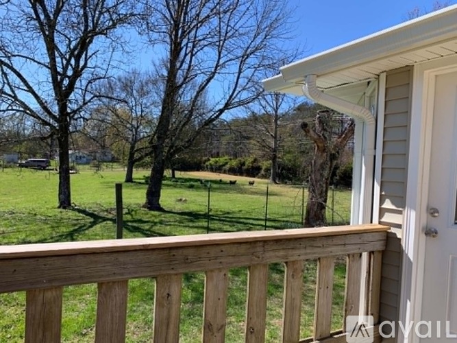 A wooden deck overlooks a grassy field with trees.