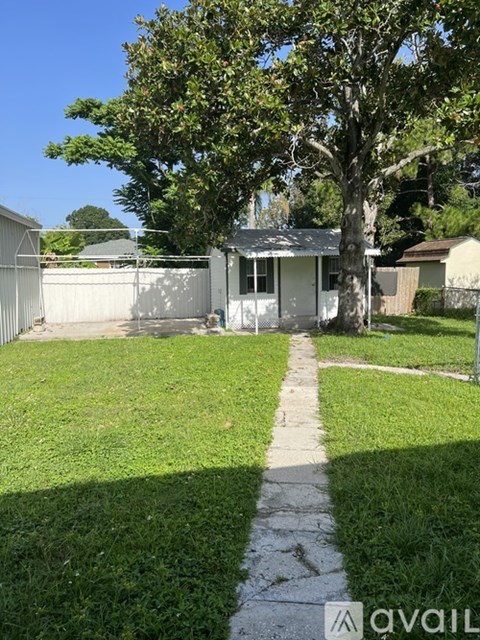 A backyard with a white house, a tree, and a fence.