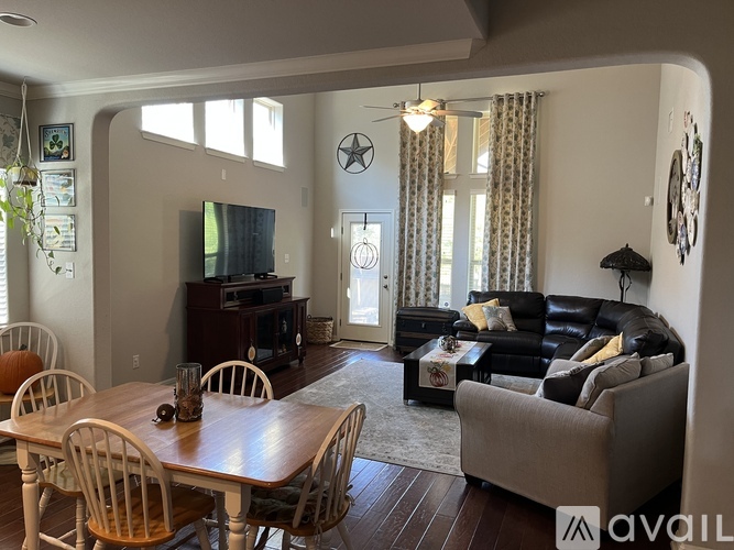 A living room with a leather couch, a wooden dining table with chairs, and a television.