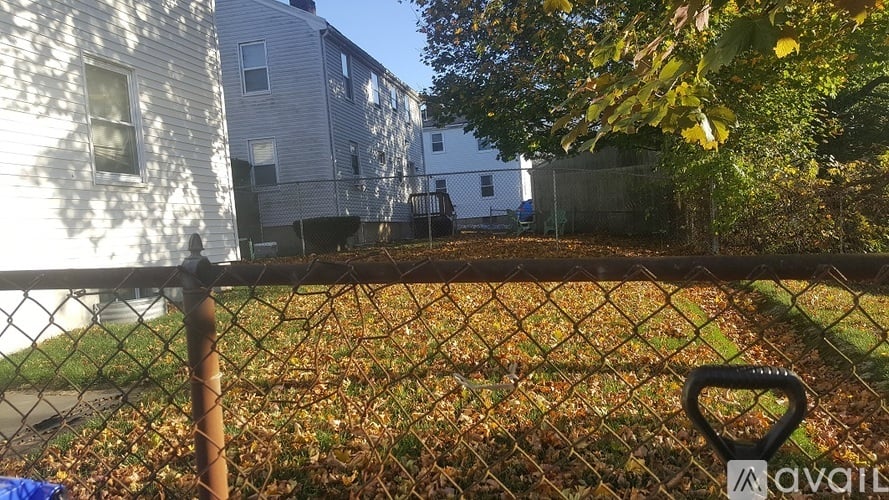 A chain link fence with a gate in front of a yard with trees and houses in the background.