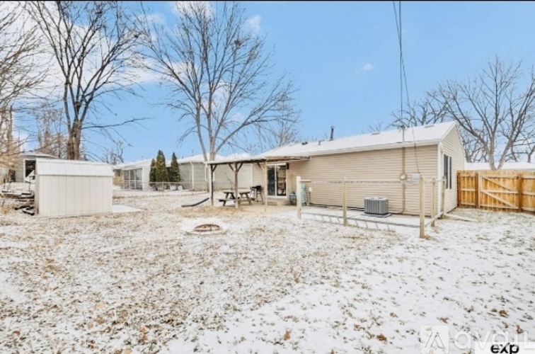A snow-covered ground with a building and a picnic table in the background.