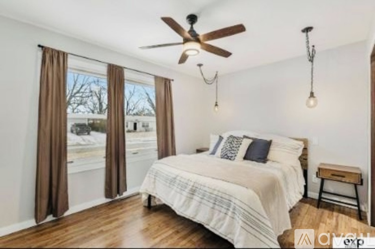 A bedroom with a bed, a ceiling fan, and a window with curtains.