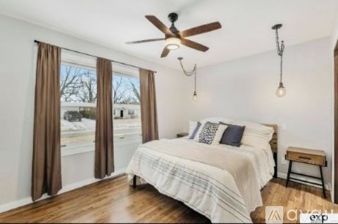 A bedroom with a bed, a ceiling fan, and a window with curtains.