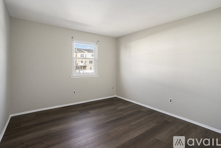 A room with wooden flooring and a window showing a building outside.