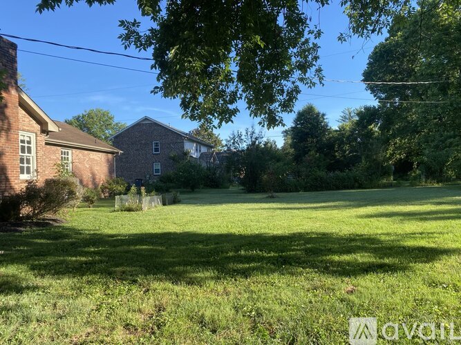 A grassy field with a house and trees in the background.