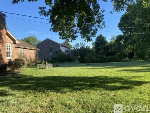 A grassy field with a house and trees in the background.