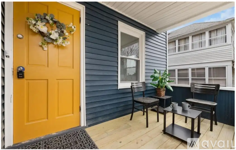 A yellow door with a wreath on it and a table with chairs on the porch.