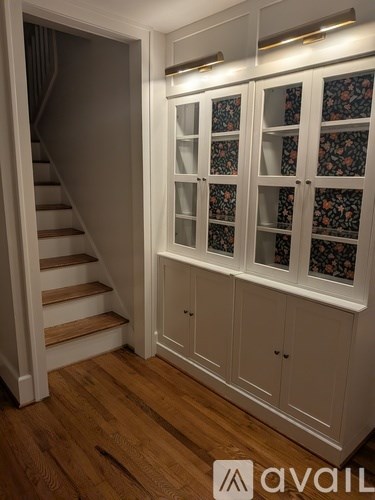 A set of stairs with a wall of cabinets with glass doors on top.