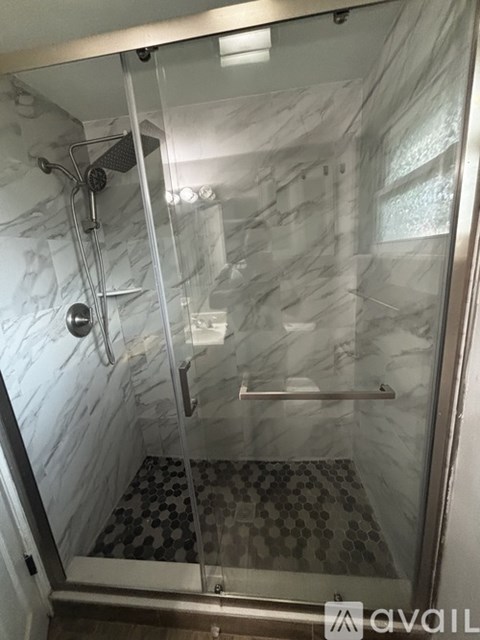 A shower with a glass door and a marble wall.