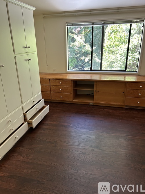 A room with wooden floors and a large window with a view of trees outside.