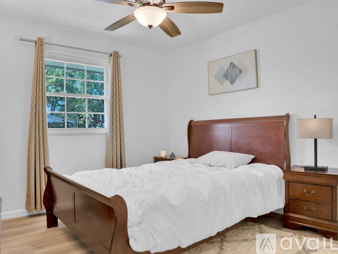 A bedroom with a large bed, a ceiling fan, and a window with curtains.