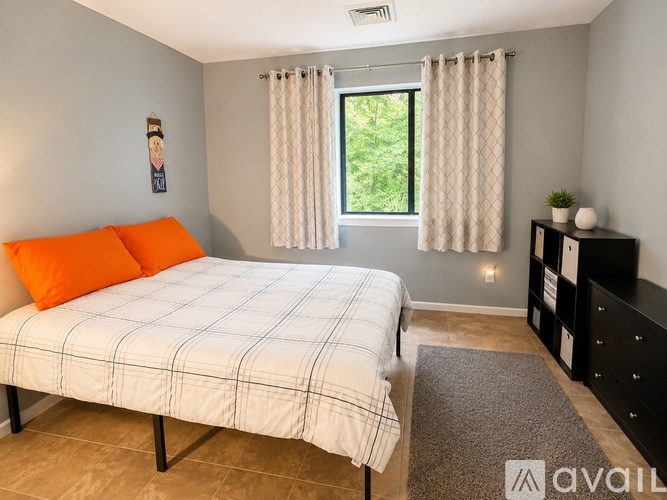 A bedroom with a bed, a nightstand, and a window with curtains.