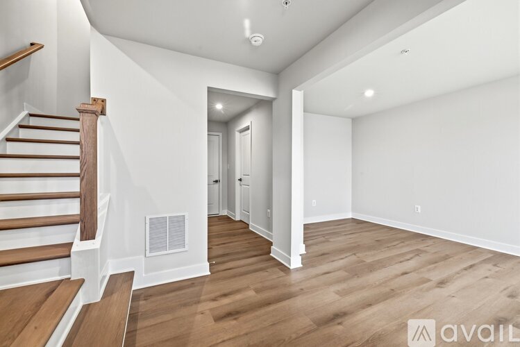 A spacious room with wooden flooring and a staircase on the left side.