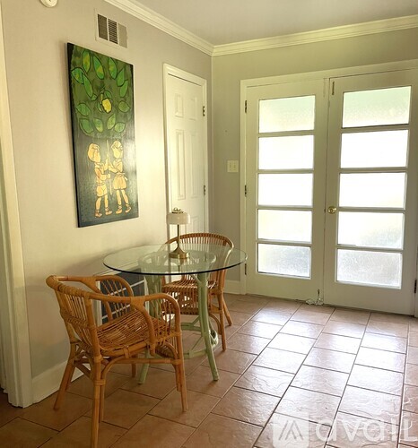 A room with a glass table and chairs and a painting on the wall.