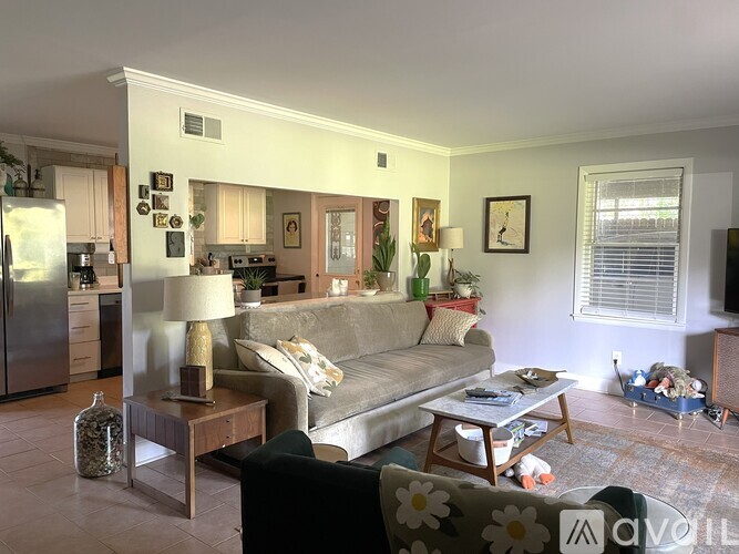 A living room with a grey couch, a coffee table, and a refrigerator in the background.
