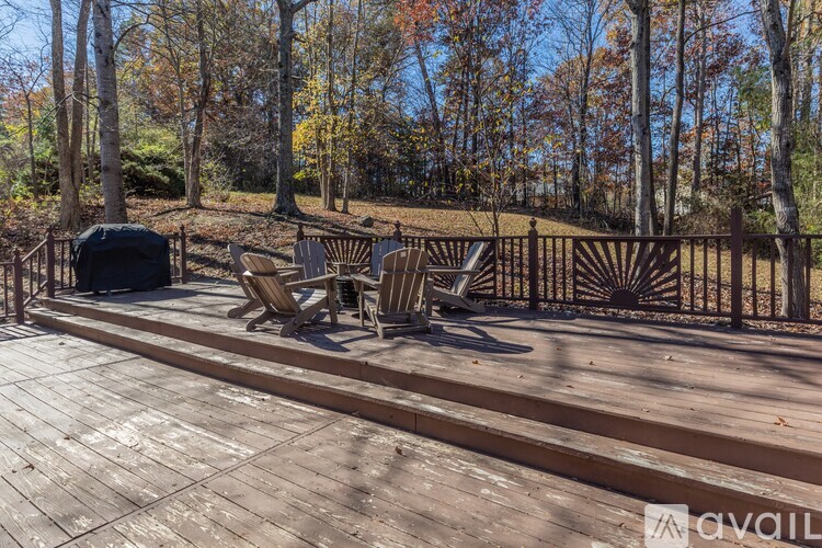 A deck with chairs and a grill surrounded by a fence and trees.