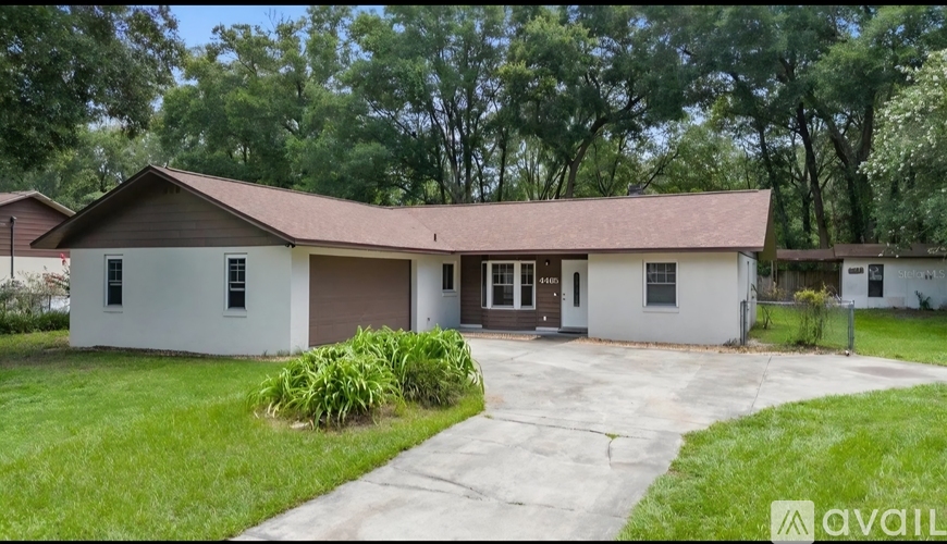 A house with a brown roof and white walls is surrounded by greenery.