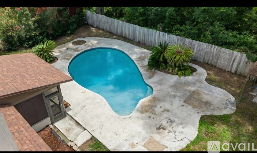 A small pool with a concrete edge and a small house with a brown roof next to it.