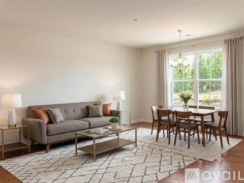 A living room with a grey sofa, a glass coffee table, and a dining table with chairs.