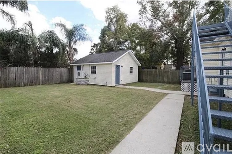 A small white house with a grey roof is surrounded by a fence and a grassy yard.
