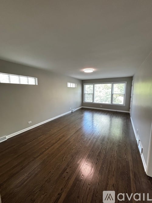 A room with wooden flooring and two windows.
