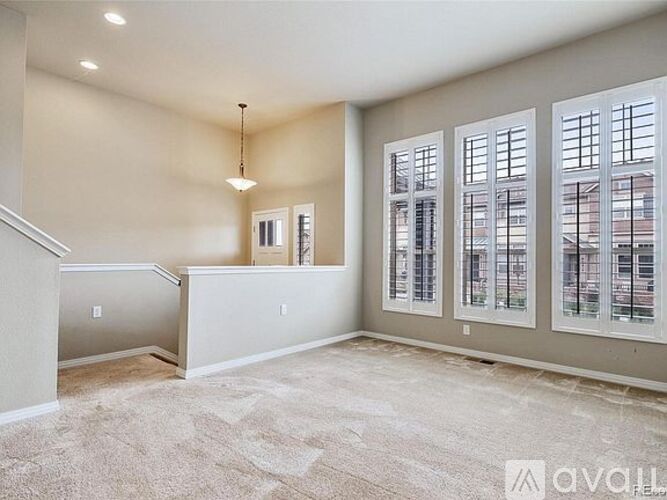 A spacious room with a carpeted floor, a staircase, and a large window with a view of a building outside.