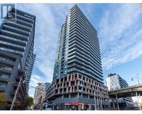 A tall building with a glass facade stands in the foreground of a city street.