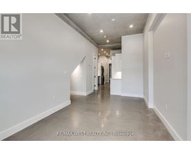 A spacious, empty room with a polished concrete floor and white walls, with a doorway leading to another room visible in the distance.