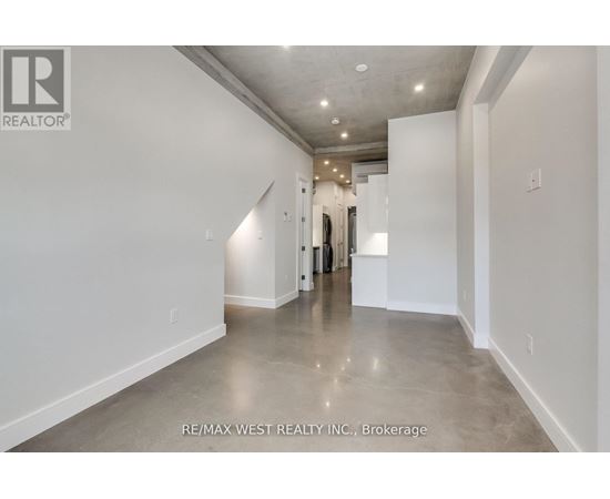 A spacious, empty room with a polished concrete floor and white walls, with a doorway leading to another room visible in the distance.