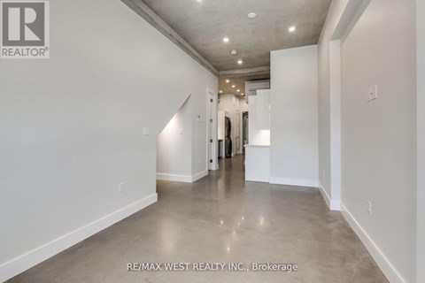 A spacious, empty room with a polished concrete floor and white walls, with a doorway leading to another room visible in the distance.