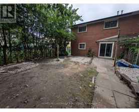 A backyard with a dirt area, a few trees, and a brick house.