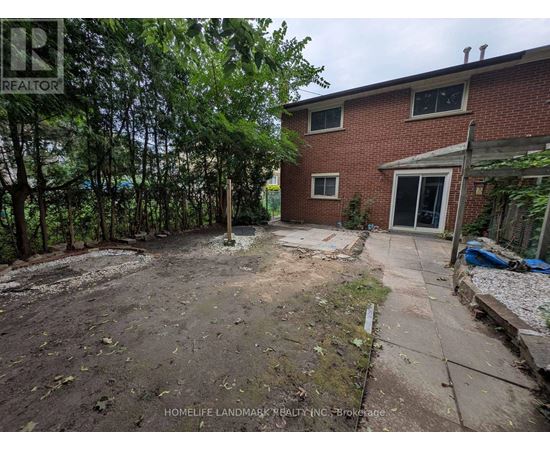 A backyard with a dirt area, a few trees, and a brick house.
