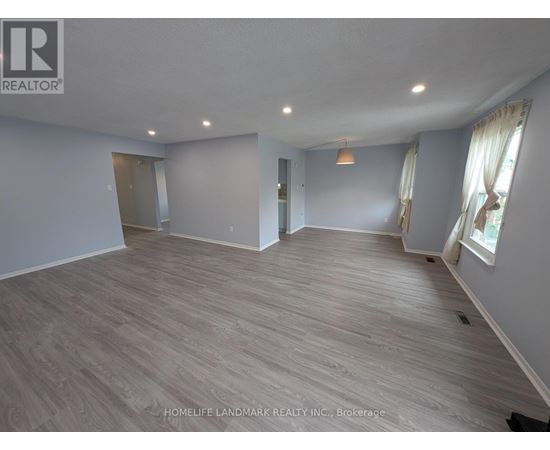 A spacious room with wooden flooring and a large window with curtains.