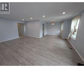 A spacious room with wooden flooring and a large window with curtains.