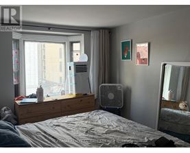 A bedroom with a bed, a window with a fan, a dresser with a laptop and a mirror.
