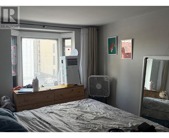 A bedroom with a bed, a window with a fan, a dresser with a laptop and a mirror.
