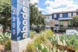 A blue and white sign with the word "abode" on it stands in front of a building.