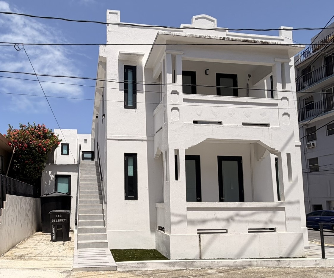 A white two-story house with a black trash bin in front.
