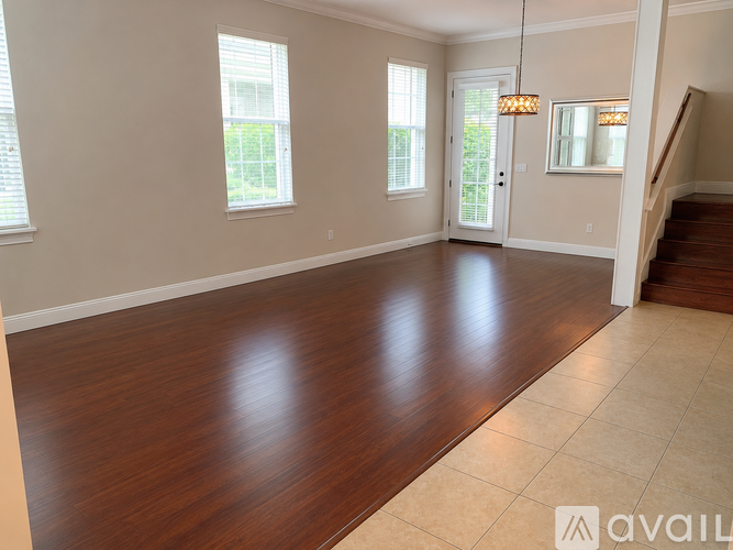 A spacious room with wooden flooring and a staircase on the right side.