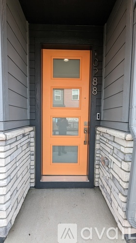 A bright orange door with a glass window is set in a grey wall.