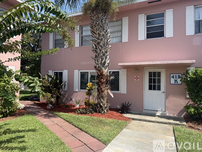 A pink building with a white door and a palm tree in front.