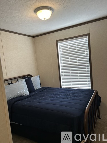 A bedroom with a bed, pillows, and a window with blinds.