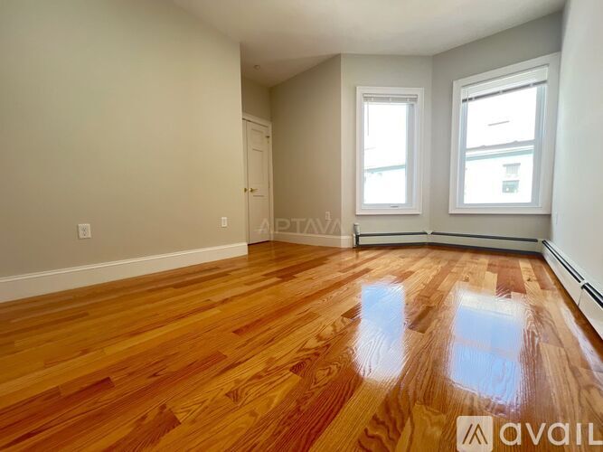 A room with wooden flooring and two windows.
